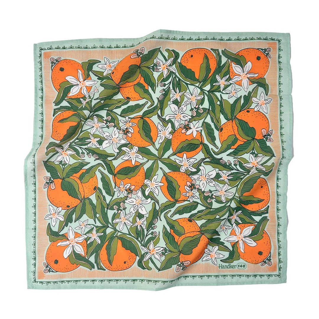 A bandana featuring an orange and citrus pattern with white flowers, bordered by a mint green patterned edge. 