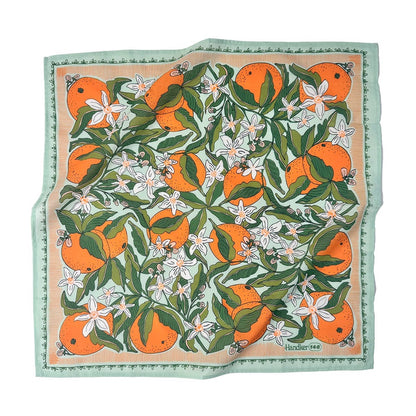 A bandana featuring an orange and citrus pattern with white flowers, bordered by a mint green patterned edge. 