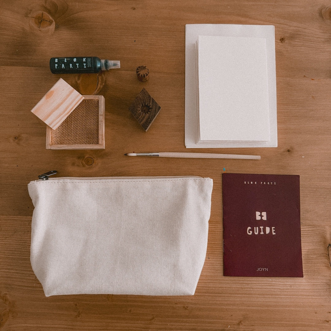 a bottle of ink, pine ink tray, 2 wooden blocks, cards, a paintbrush, canvas pouch, and block printing guide on a table 