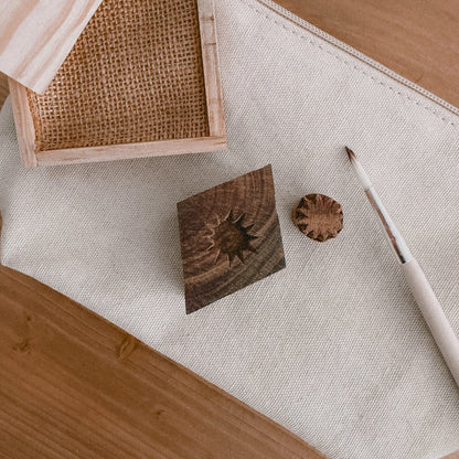 close up of a pine ink tray, paintbrush, and 2 wooden block stamps on a canvas pouch