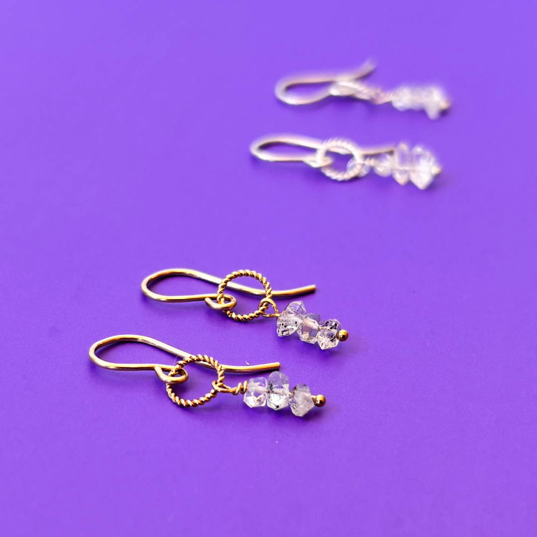 Pair of gold and silver earrings with herkimer diamonds on a purple background