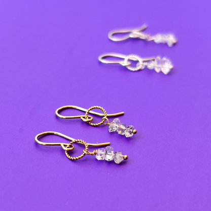 Pair of gold and silver earrings with herkimer diamonds on a purple background