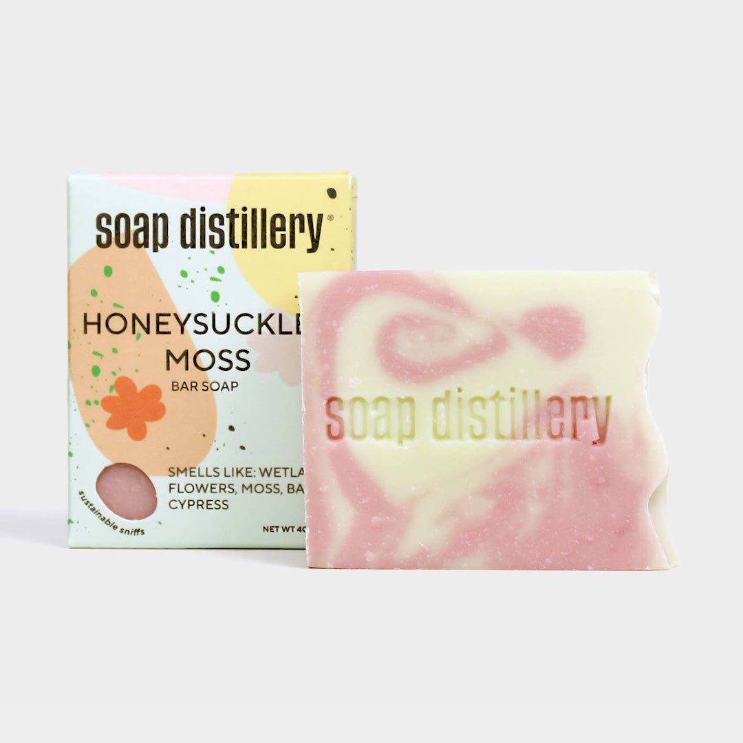Bar of honeysuckle and moss scented soap with packaging labeled 'Soap Distillery' on a white background