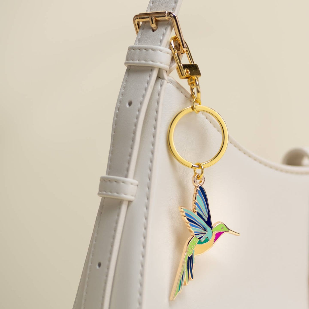 Colorful hummingbird keychain attached to a white purse strap with a gold clasp.