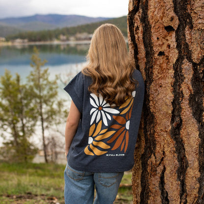 Person wearing a floral-patterned shirt leaning against a tree with a scenic lake view.