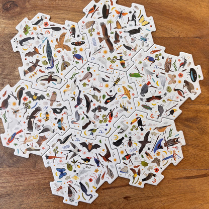 A collection of white jigsaw puzzle pieces featuring detailed illustrations of various birds and nature motifs, arranged in a circular pattern on a wooden surface.