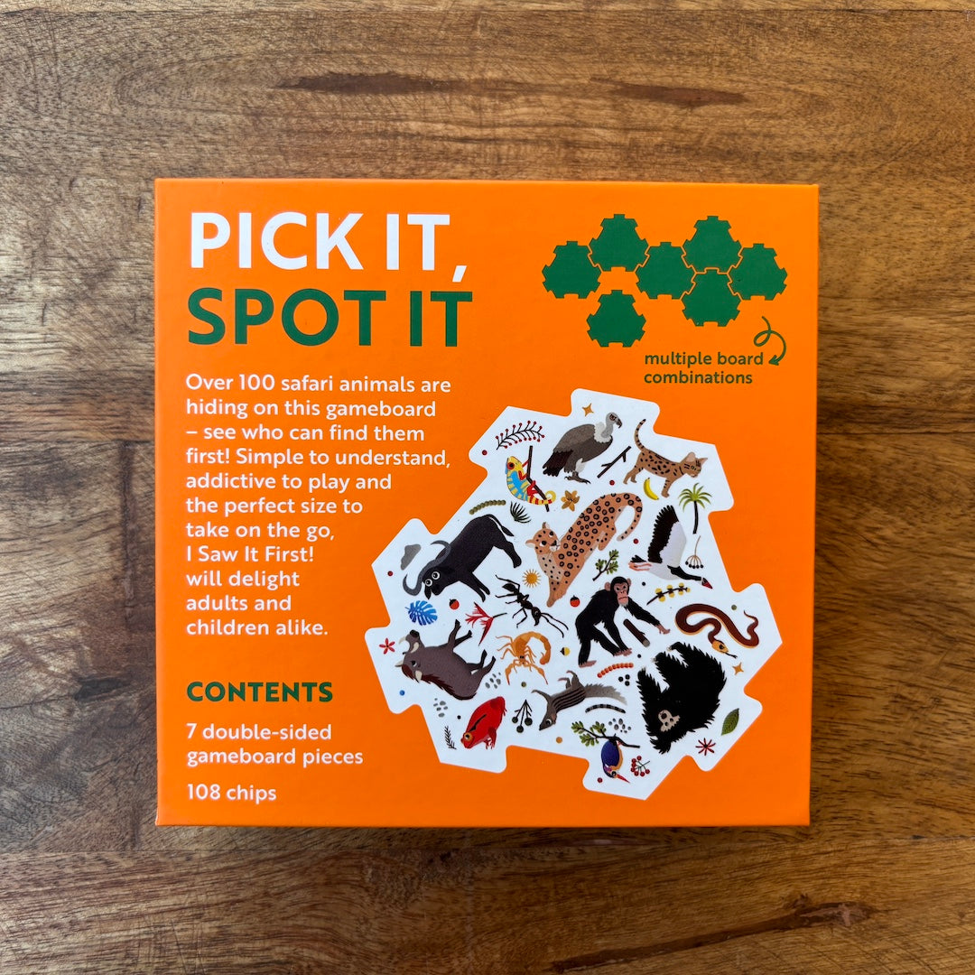 The back of the orange packaging box for the 'I saw it first safari!' board game lies flat on a rustic wooden tabletop. The box features white and green text, an illustration of various safari animals on a gameboard, and lists the contents: 7 double-sided gameboard pieces and 108 chips.