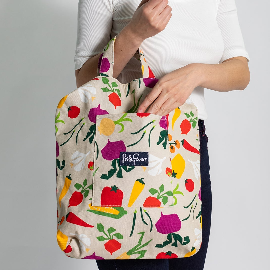 Tote bag with colorful vegetable pattern held by a person against a gray background