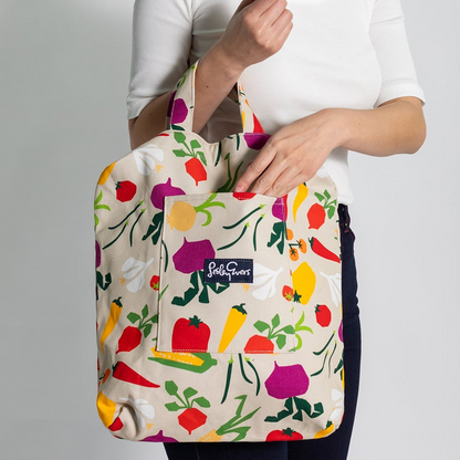Tote bag with colorful vegetable pattern held by a person against a gray background