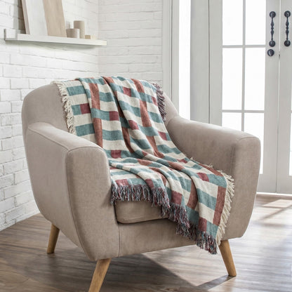 A beige upholstered armchair with light wood legs in a bright room, draped with a fringed throw blanket featuring a muted plaid pattern in cream, teal, and terracotta.