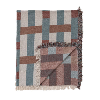 A woven throw blanket with a geometric block pattern in muted tones of slate blue, terracotta, dusty rose, and cream, featuring fringed edges and shown folded on a white background.