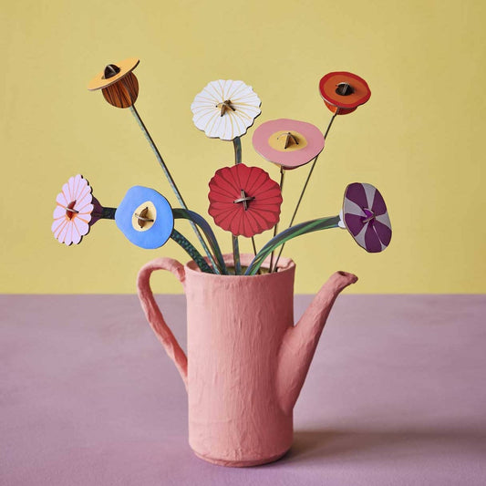 Pink teapot with colorful cardboard flowers against a yellow background