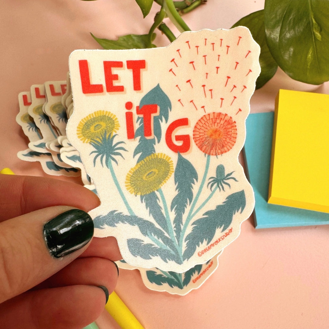 Hand holding a 'Let It Go' sticker with dandelion design on a colorful background