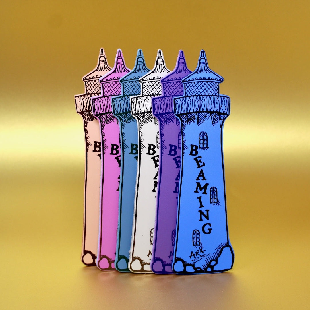 Five colorful lighthouse-shaped bookmarks in pink, purple, blue, and white, lined up on a yellow gradient background. The frontmost lighthouse is blue with black outlines and the word 'BEAMING' written vertically.