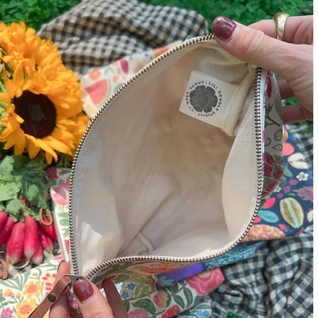 Colorful floral-patterned bag with a brand label, held open by hands against a natural background.