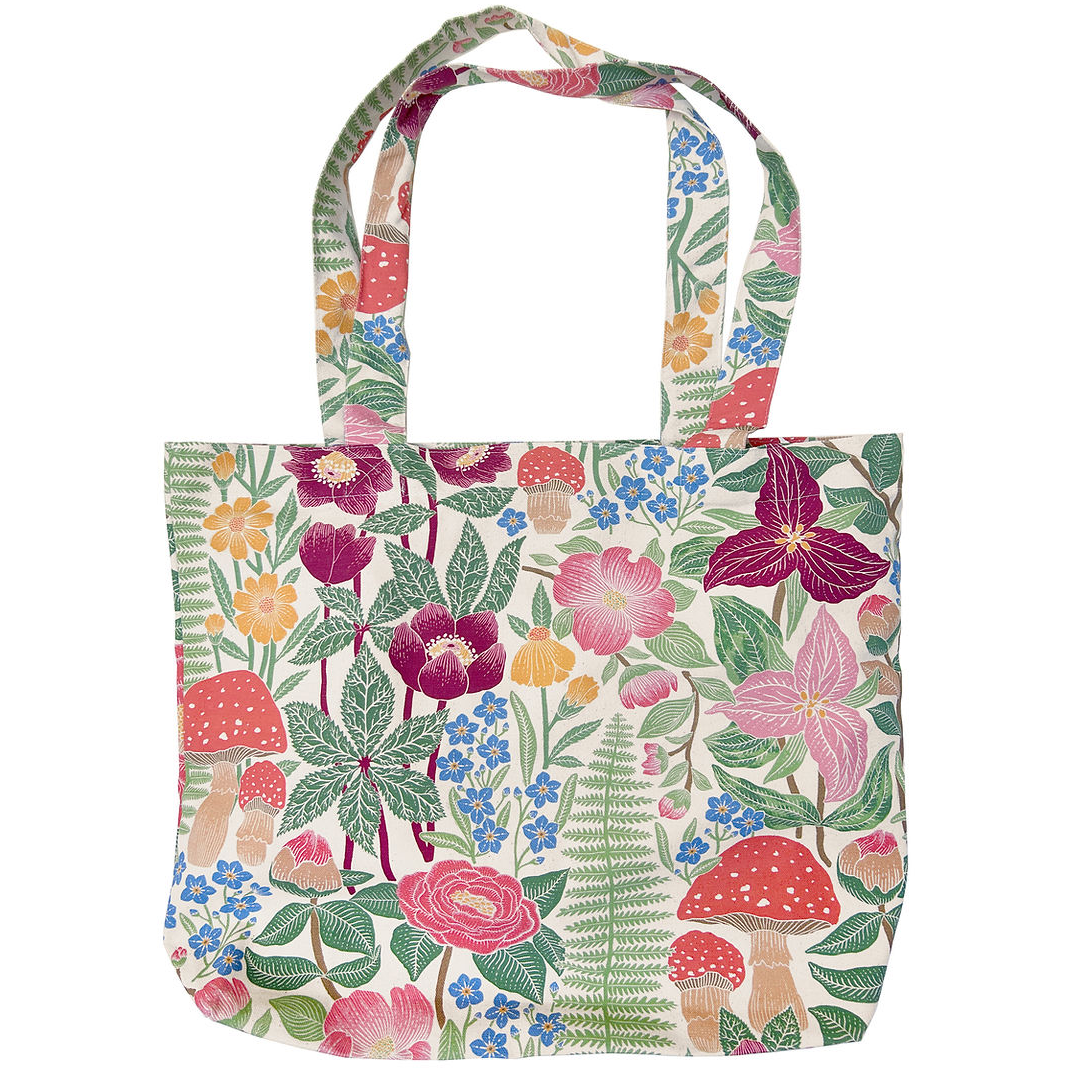 A canvas tote bag featuring a dense, colorful botanical and mushroom print on a cream background, complete with two shoulder straps, shown against a plain white background.