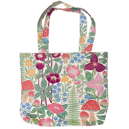 A canvas tote bag featuring a dense, colorful botanical and mushroom print on a cream background, complete with two shoulder straps, shown against a plain white background.