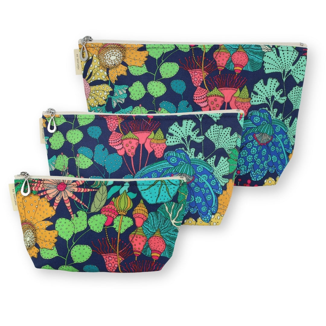 Three fabric zip pouches in a nested set, featuring a vibrant botanical pattern with pink flowers, green leaves, and yellow sunflowers on a dark navy blue background, set against a plain white background.