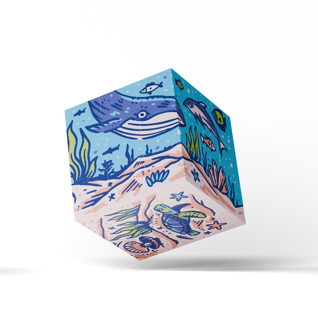 A 3D cube-shaped product with an illustrated ocean floor design, featuring a blue whale, sea turtle, fish, and coral in blue, teal, beige, and green tones, shown floating against a white background.