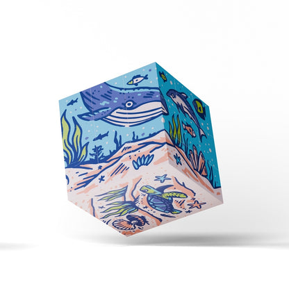 A 3D cube-shaped product with an illustrated ocean floor design, featuring a blue whale, sea turtle, fish, and coral in blue, teal, beige, and green tones, shown floating against a white background.