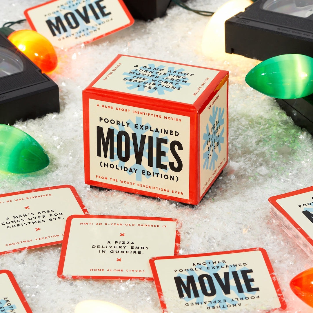 Card game box titled 'Poorly Explained Movies Holiday Edition' with cards on a textured surface.