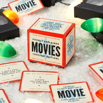 Card game box titled 'Poorly Explained Movies Holiday Edition' with cards on a textured surface.