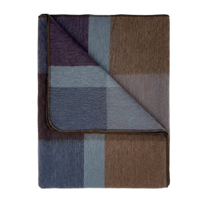 A folded plaid blanket with a textured woven surface, featuring blocks of brown, slate blue, lavender purple, and gray, shown on a plain white background.