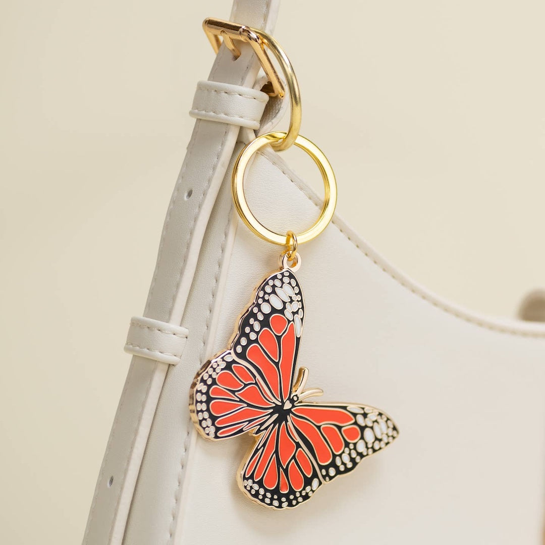 Monarchy Butterfly keychain attached to a white purse strap on a light beige background