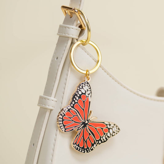 Monarchy Butterfly keychain attached to a white purse strap on a light beige background