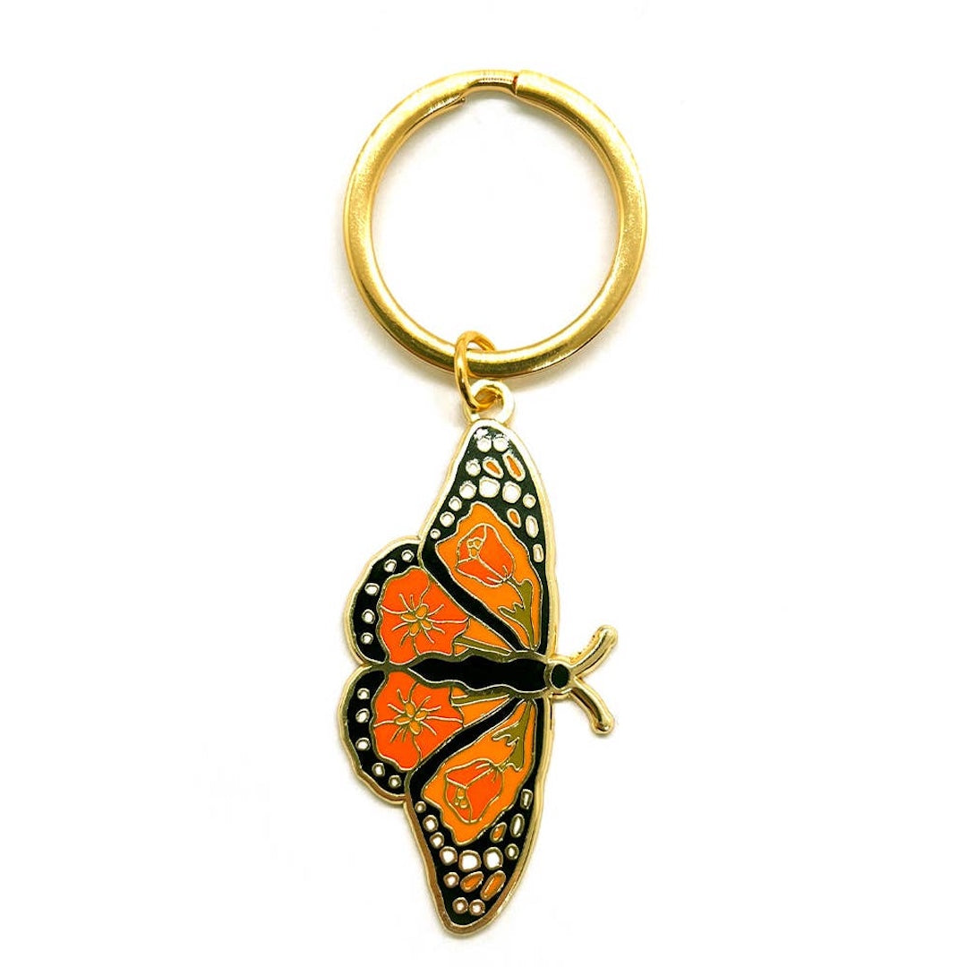 A gold-colored metal butterfly keychain with vibrant orange and black enamel detailing, attached to a split key ring, shown on a plain white background.