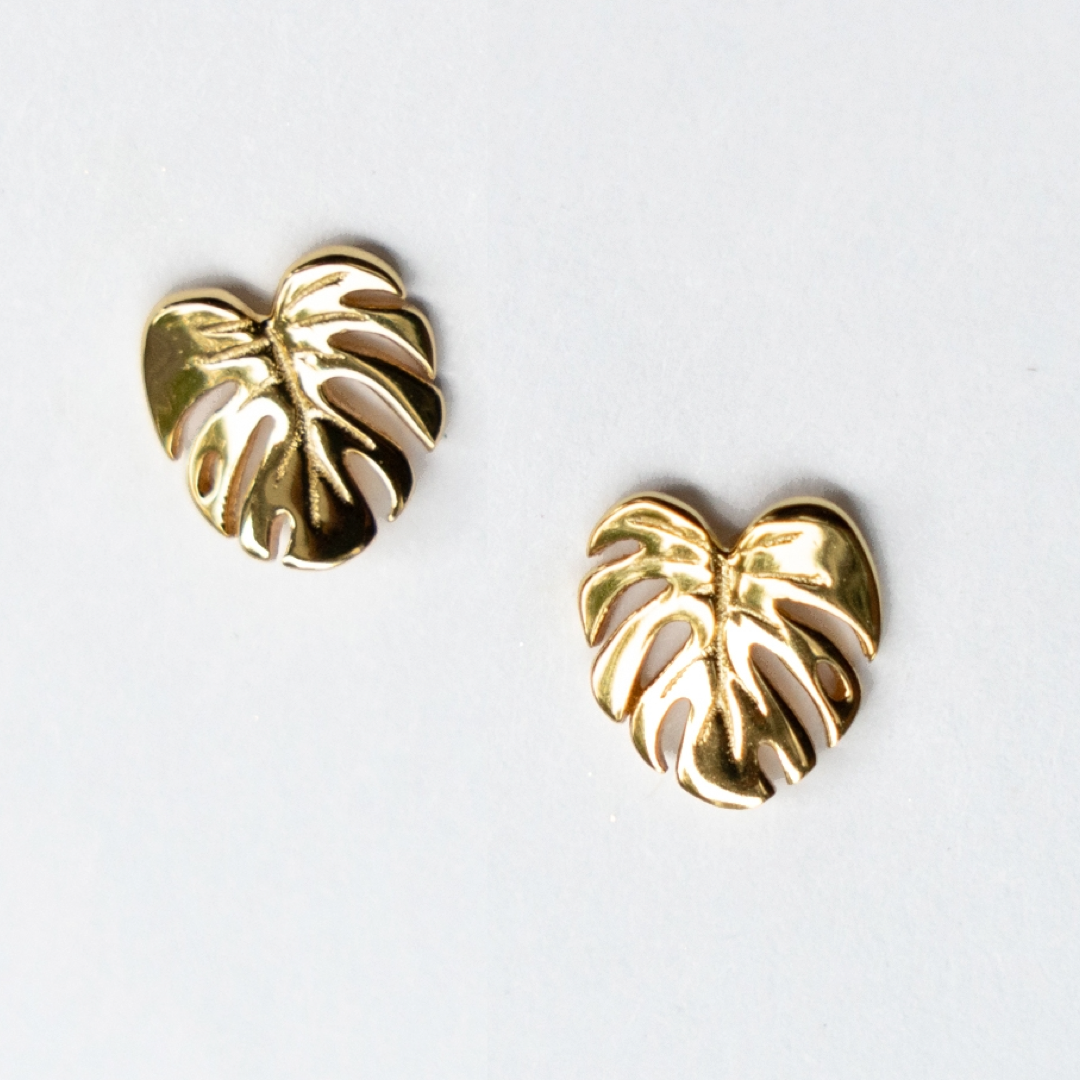 Gold monstera leaf-shaped earrings on a white background