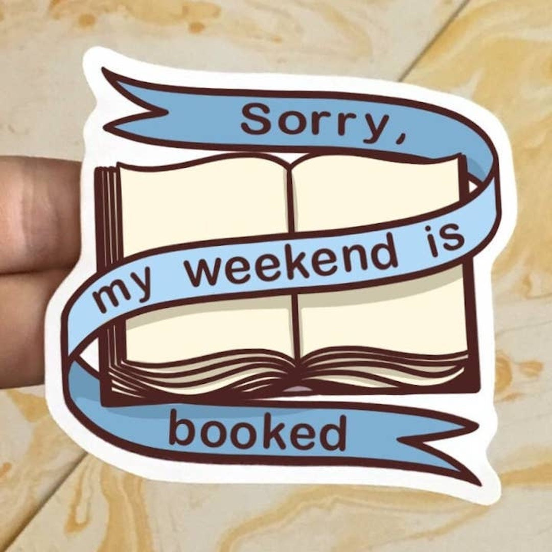 Sticker of a book with 'Sorry, my weekend is booked' text on a wooden surface