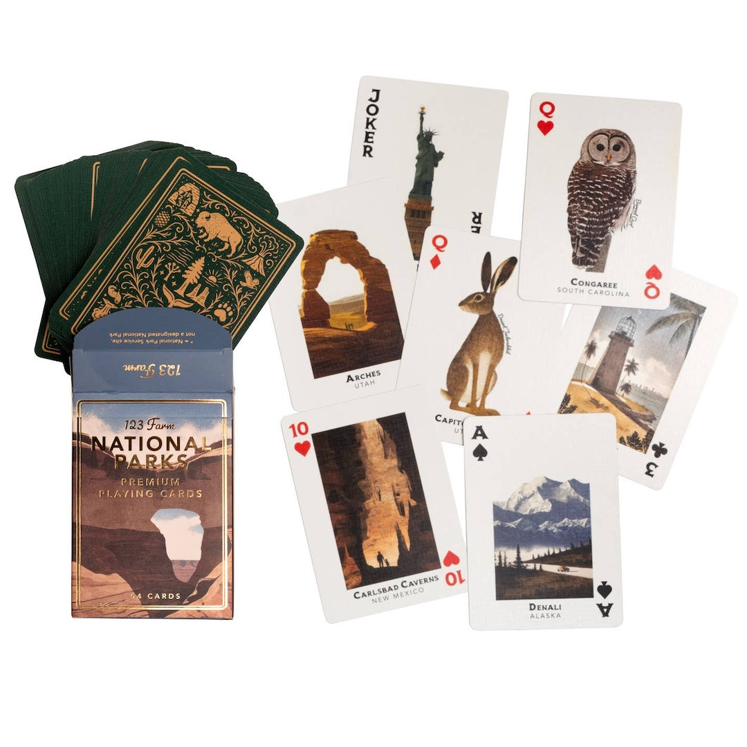 National Parks playing cards set with a blue and brown illustrated box, a fanned deck of green-backed cards, and several sample cards showing national park illustrations on a white background.