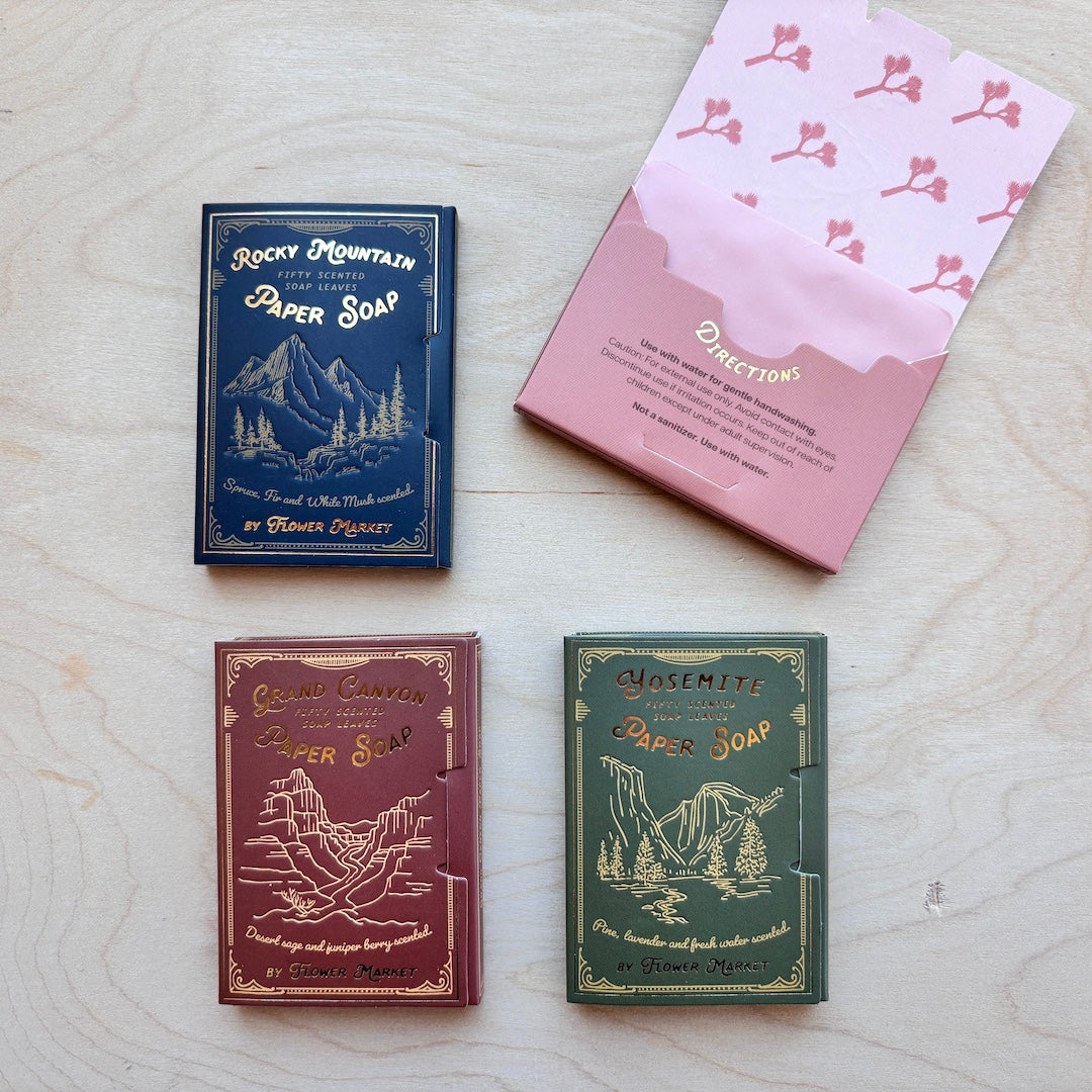 Four vintage-style paper soap boxes arranged on a light wood surface, with one pink box open to show the contents. The boxes are labeled Rocky Mountain, Grand Canyon, Yosemite, and Yellowstone, with mountain and canyon illustrations on each.