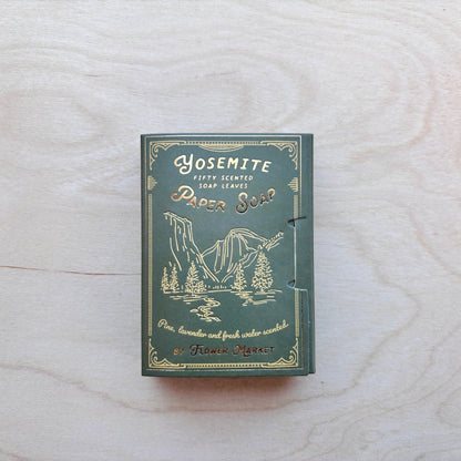 A vintage-style soap box labeled 'Yosemite Scented Paper Leaves' in muted green with gold embossed lettering and mountain artwork, placed on a light wood surface.