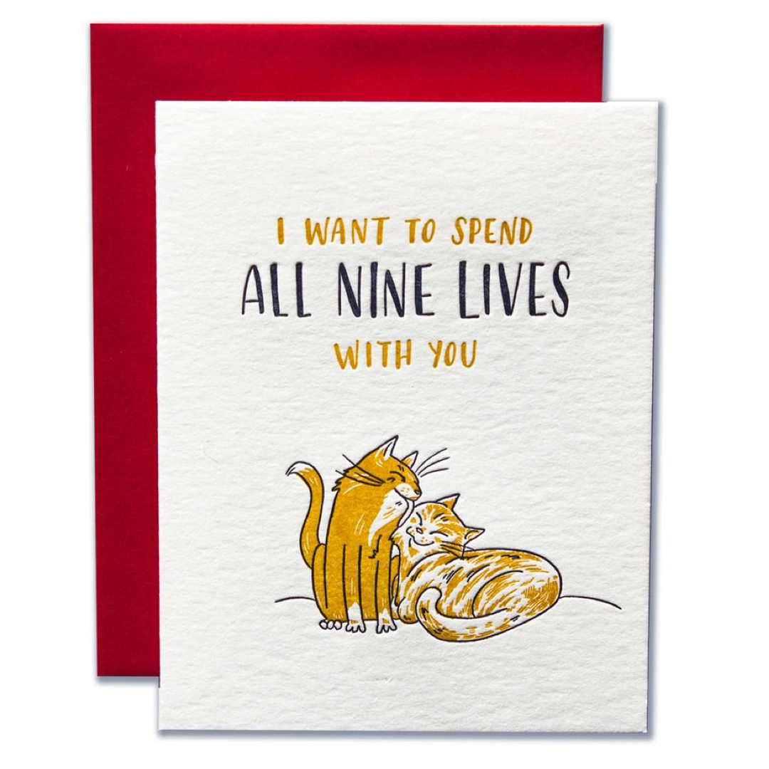 A white greeting card with a red envelope behind it, featuring the text 'I WANT TO SPEND ALL NINE LIVES WITH YOU' and an illustration of two orange cats on a white textured background.