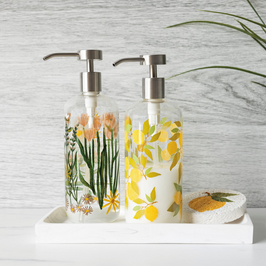 Two soap dispensers with floral and lemon designs on a marble surface.