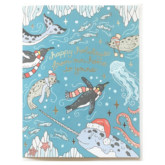 A square holiday greeting card featuring an underwater winter scene with penguins, seals, a narwhal, octopus, jellyfish, fish, and stars on a light blue background. Gold script reads 'happy holidays from our home to yours.