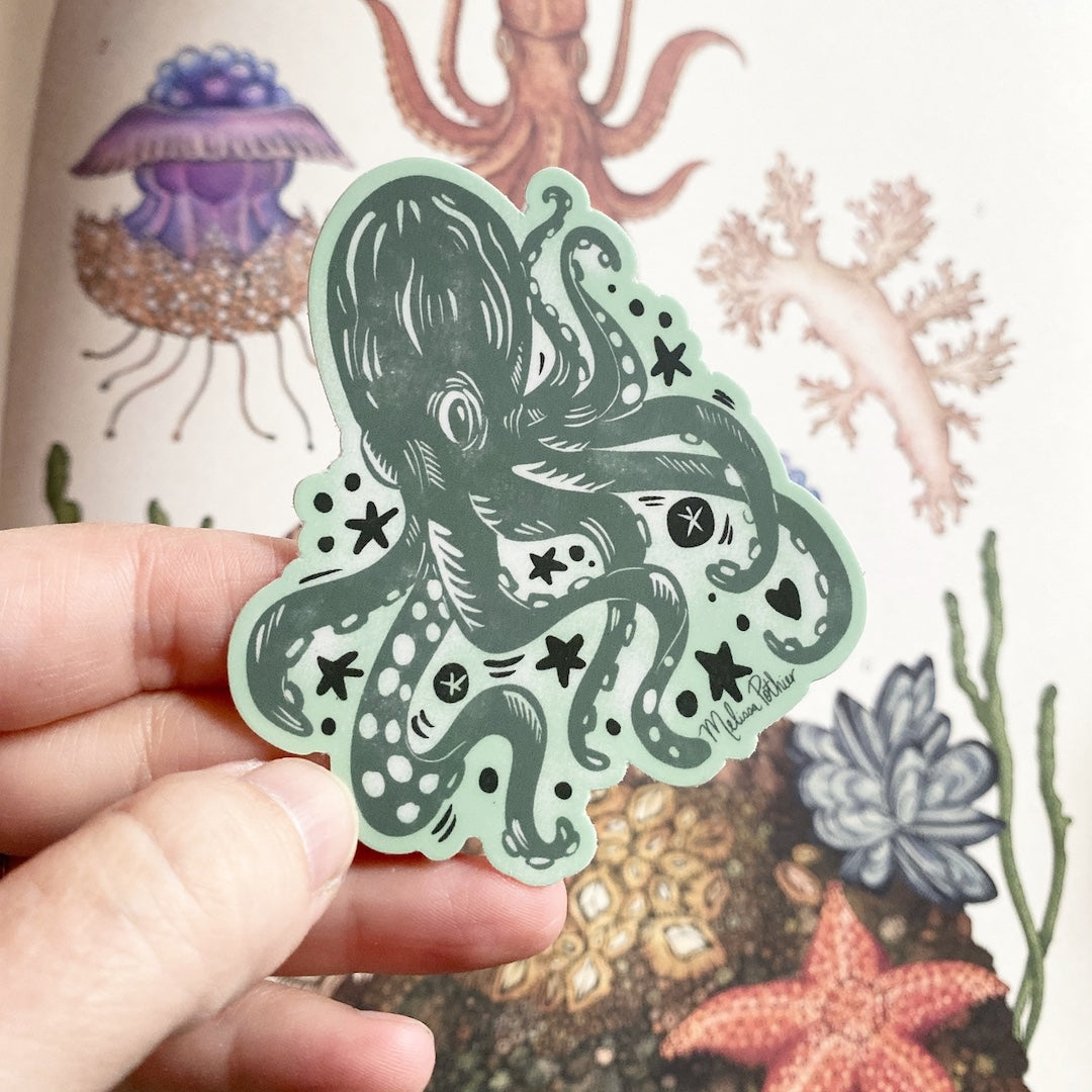 Hand holding a green octopus sticker with a colorful underwater background