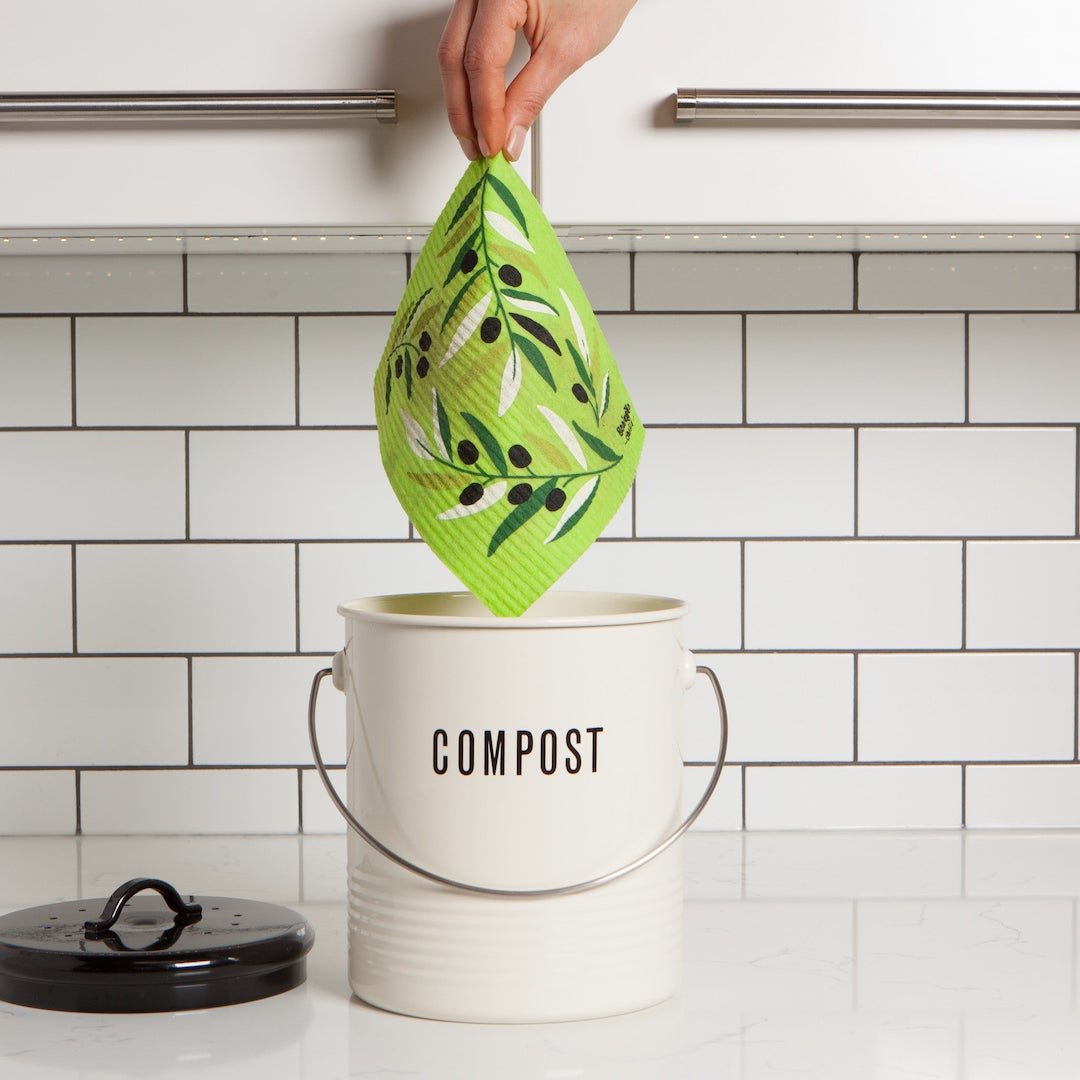 Person putting a swedish dishcloth into a white compost bin with a black lid on a kitchen counter.