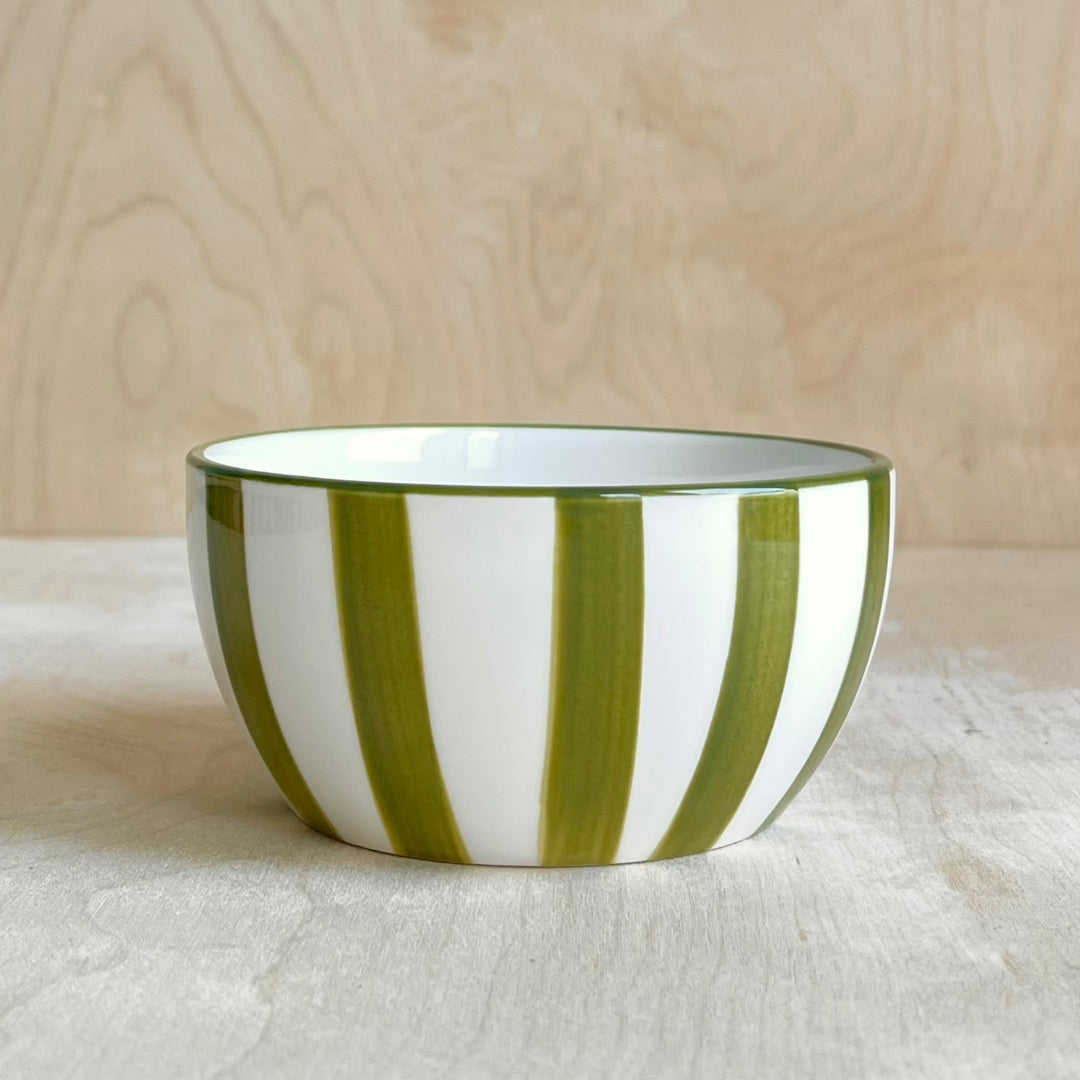 Ceramic bowl with olive green and white stripes on a wooden surface 