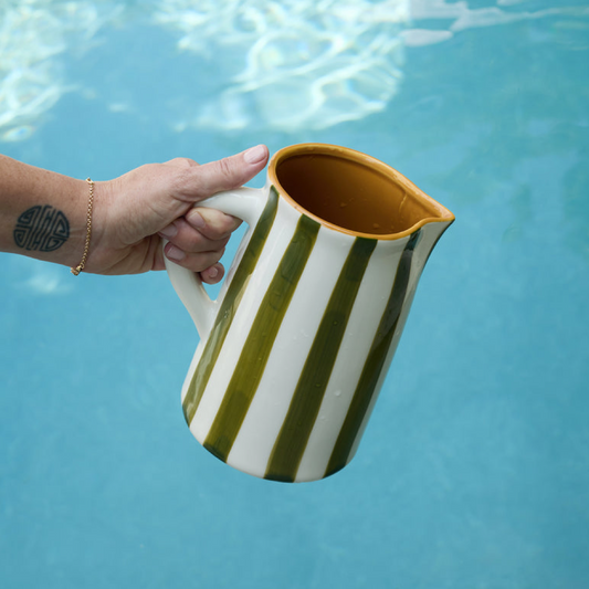 Hand holding a green and white striped pitcher against a blue water background