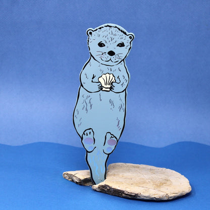 bookmark shaped like an otter holding a shell on a blue background