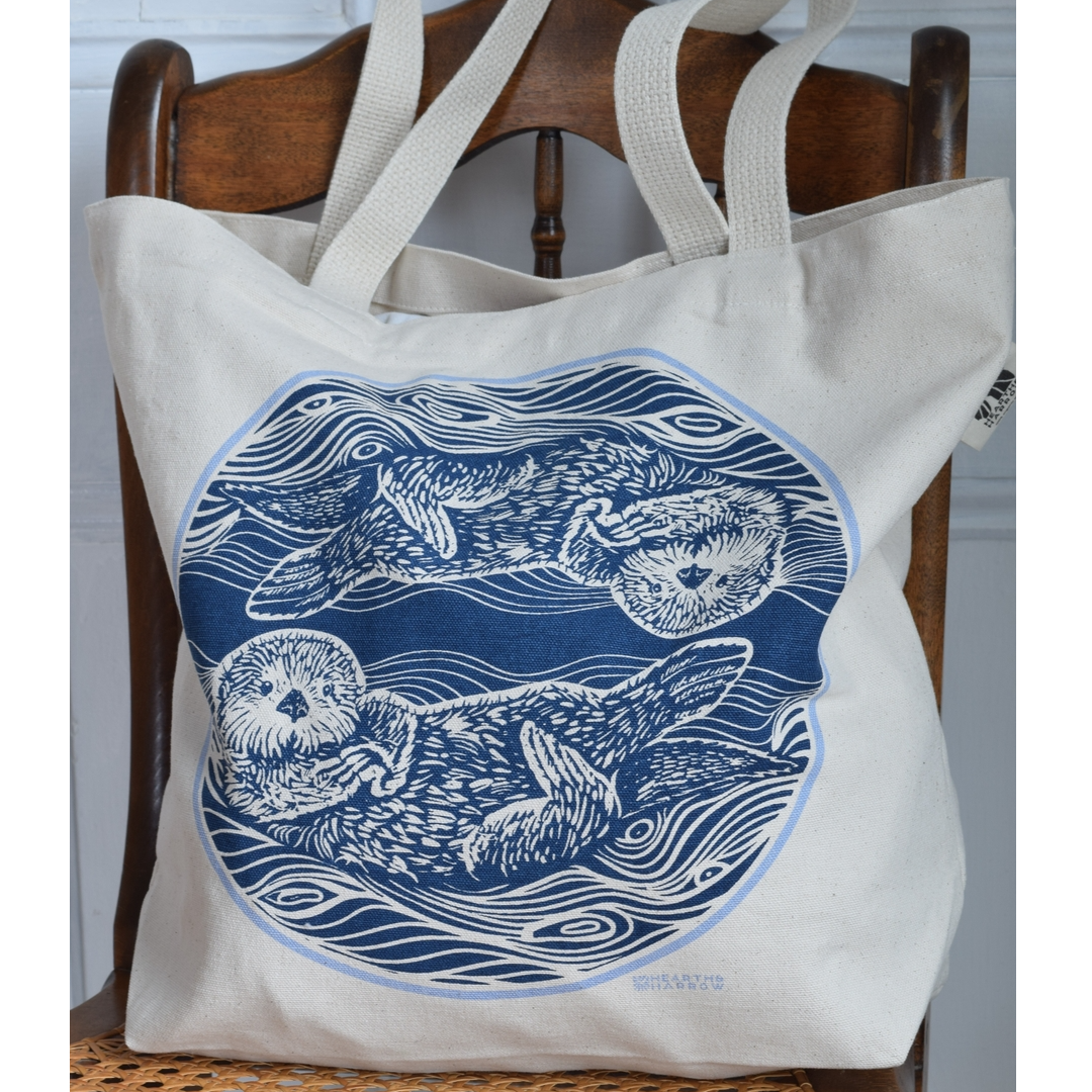 canvas tote bag with two otters in the water printed in blue on the tote