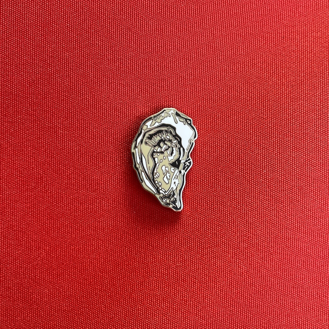 A small silver-toned oyster-shaped pin placed on a textured red fabric background.