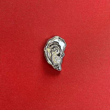 A small silver-toned oyster-shaped pin placed on a textured red fabric background.