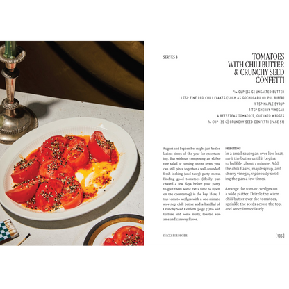 A cookbook page showing the text 'TOMATOES WITH CHILI BUTTER & CRUNCHY SEED CONFETTI' with ingredients, directions, and photos of prepared tomato dishes on a tabletop.