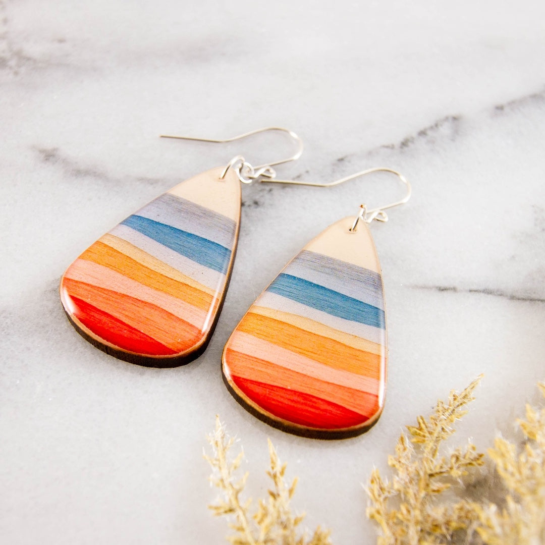 Teardrop-shaped earrings with multicolored stripes on a marble surface.