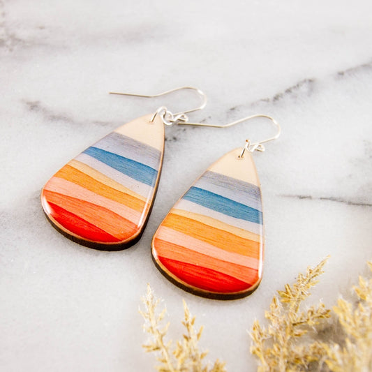 Teardrop-shaped earrings with multicolored stripes on a marble surface.