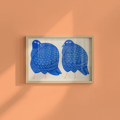A framed art print featuring two stylized blue pigeons on a white background, hung on a peach-colored wall with soft diagonal shadows.